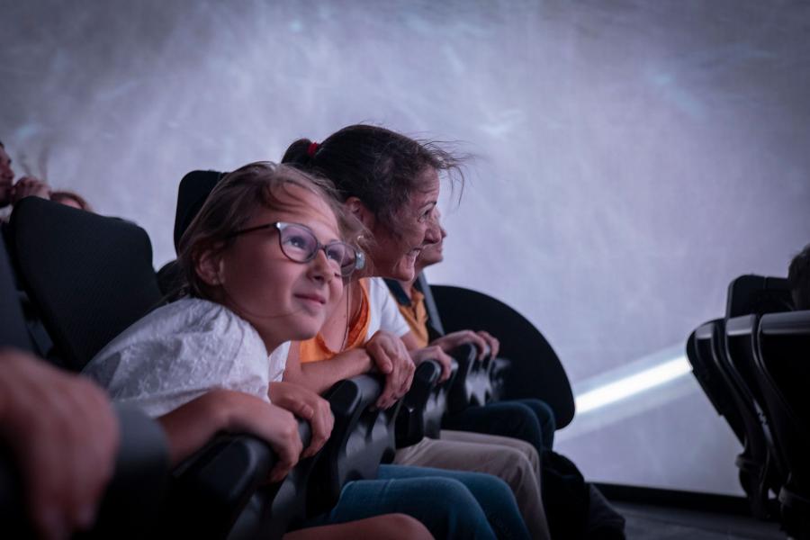A family, with child in center frame of picture, hanging on the safety bars inside Futuroscope's Chasseurs de Tornades attraction