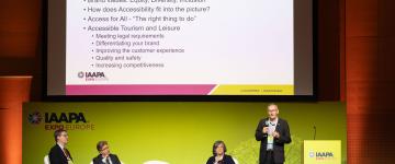 Les panélistes sur scène avec un diaporama PowerPoint sur un écran de projection montrant des questions sur le tourisme accessible lors de l'IAAPA Expo Europe