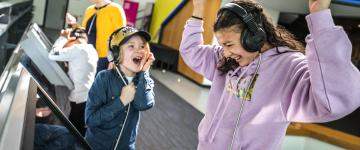 Deux enfants applaudissent une exposition tout en portant des écouteurs.