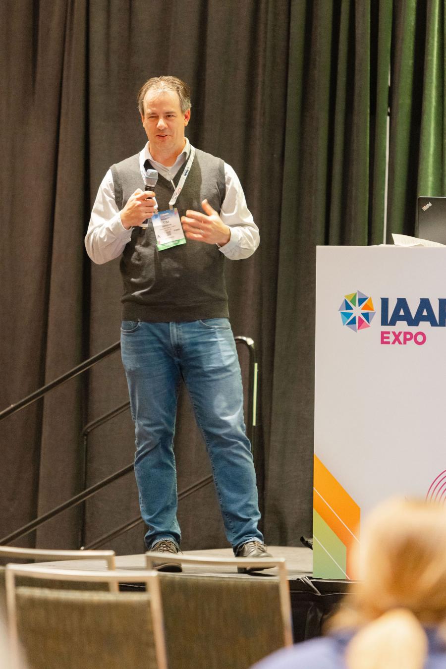 Tim Benson, chief operating officer at Fremont Family YMCA, stands next to a podium with microphone in hand, delivering his presentation during Breaking Down the Silos 2.0 EDUSession at IAAPA Expo 2023