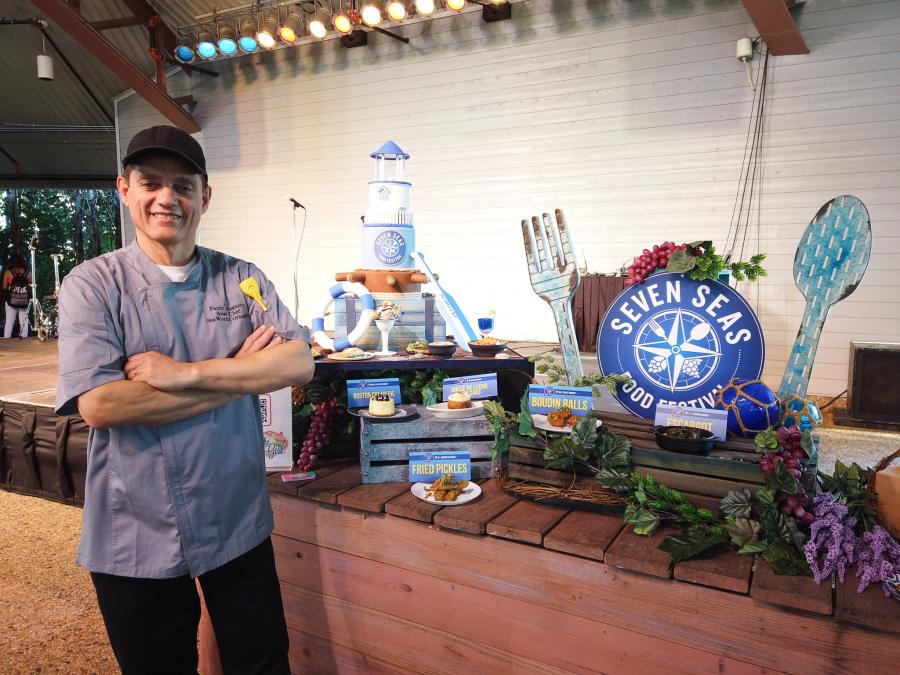 Portrait of Paulo Augusto, Brazilian sous chef at SeaWorld Orlando, posing next to the theme park's Seven Seas Food Festival promotional logo and food samples