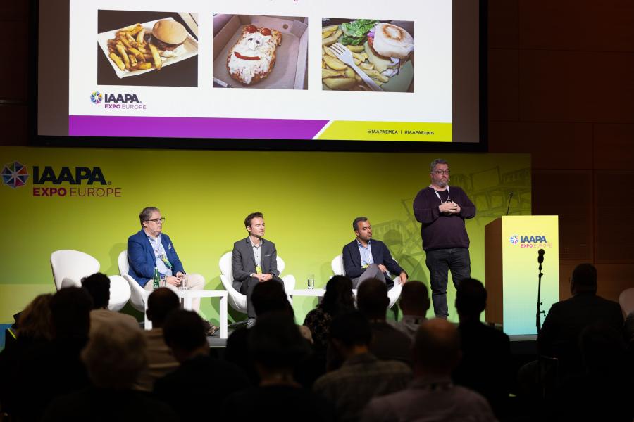 Panelists on stage with a PowerPoint slideshow on a projector screen showing food and beverage offerings as example during F&B Innovations panel at IAAPA Expo Europe
