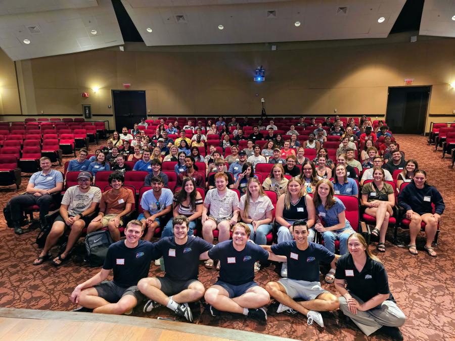 A group of students from UCF's college chapter of Future Theme Park Leaders Association (FTPLA) posing for a photo inside a university auditorium