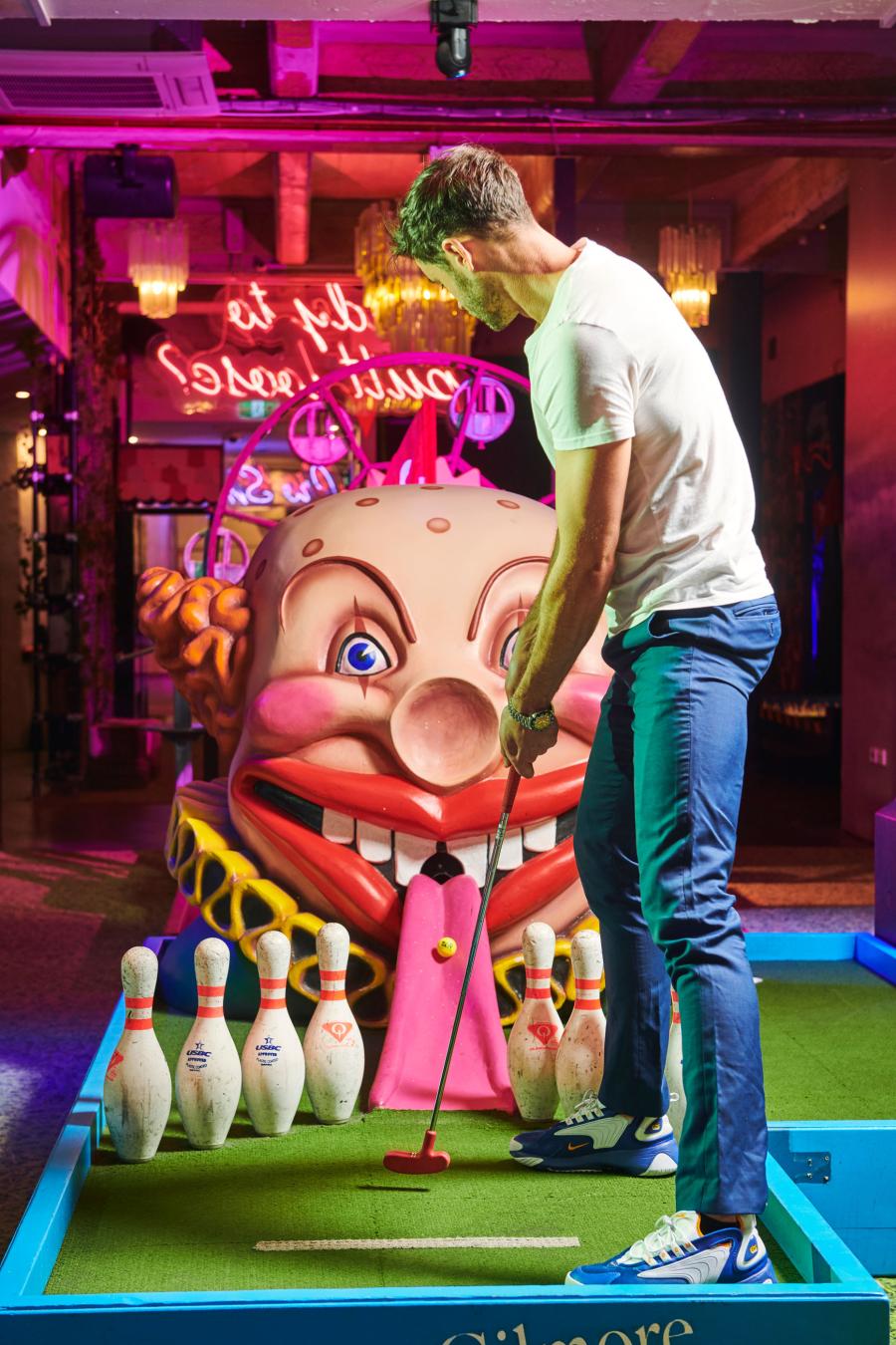 A mini golf player hit a mini golf that's going toward a wacky caricature with a wide mouth as an opening shot for a mini golf course at Holey Moley, a Funlab FEC brand