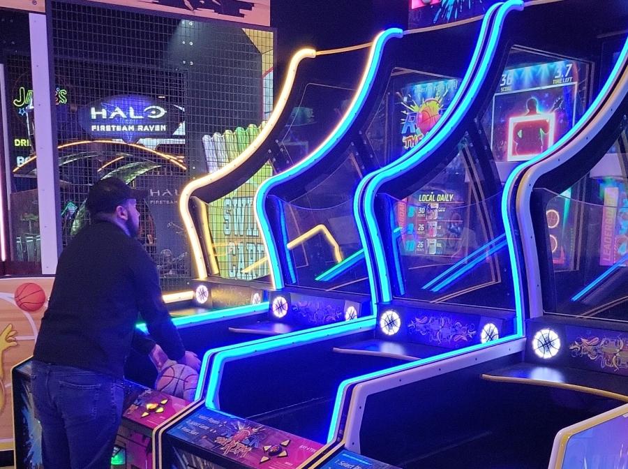Man plays basketball at a neon-lit arcade.