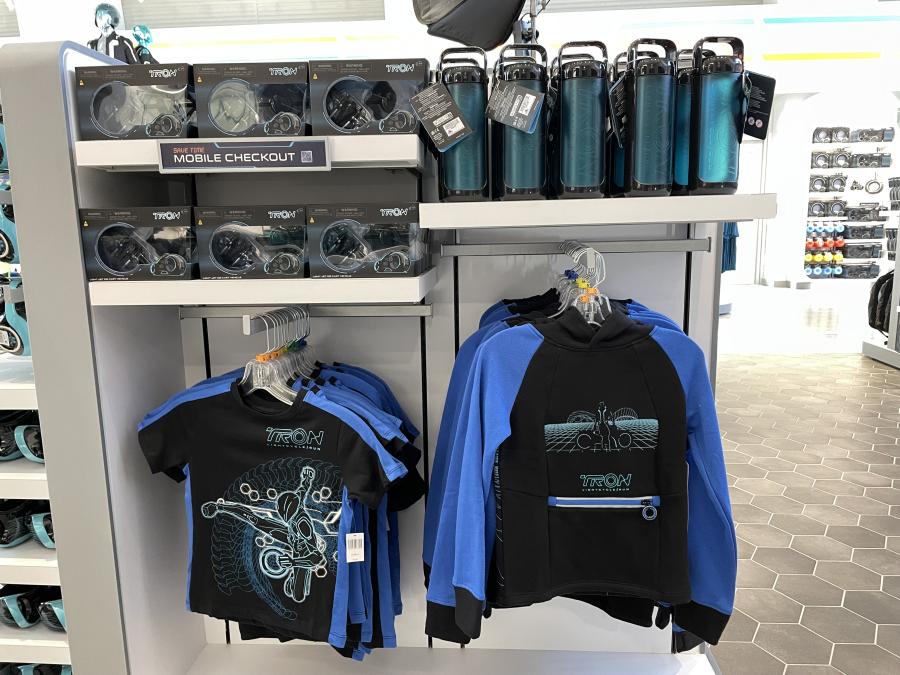 A shirt, a sweatshirt, a toy Lightcycle, and water bottles being sold on shelves in the gift shop.