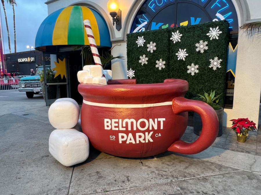 A decorative prop for social media-ready holiday photos, featuring a winter backdrop and hot cocoa mug with visible Belmont Park logo