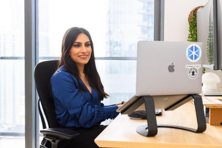 Illumix 首席执行官 Kirin Sinha 的专业肖像，她在办公桌前使用可见的 MacBook 笔记本电脑工作