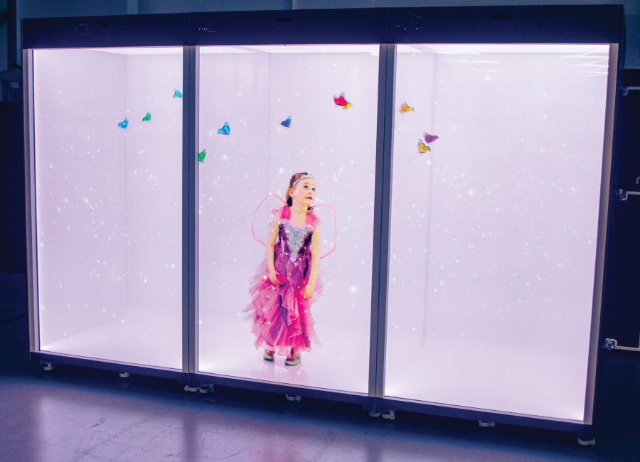 Un écran holographique carré à trois grilles avec une image 3D d'une petite fille portant une robe de fée et des ailes, regardant des papillons holographiques.