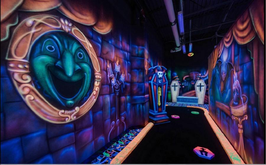 A black light mini gold course with spooky faces on the wall.