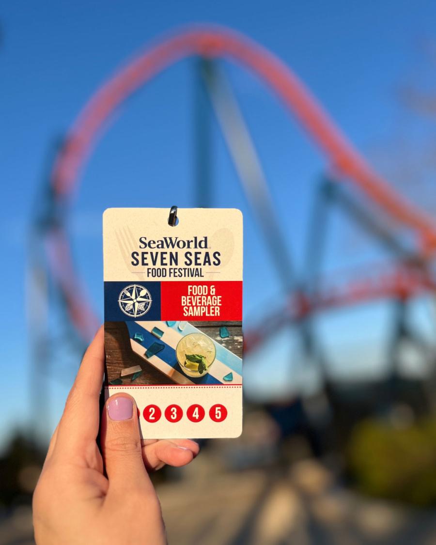 Hand holding a food sample lanyard for Seven Seas Food Festival with roller coaster in background at SeaWorld Orlando