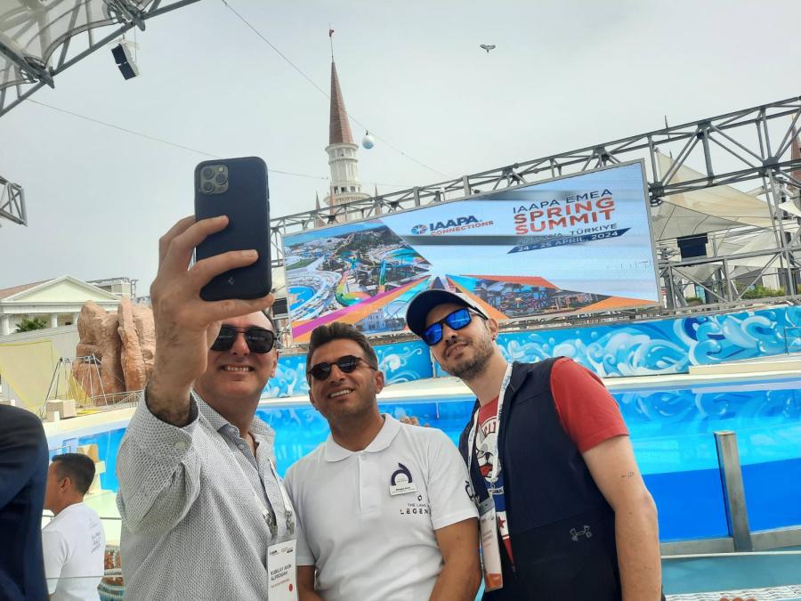 Three attendees take selfie in front of IAAPA screen and aquarium pool.
