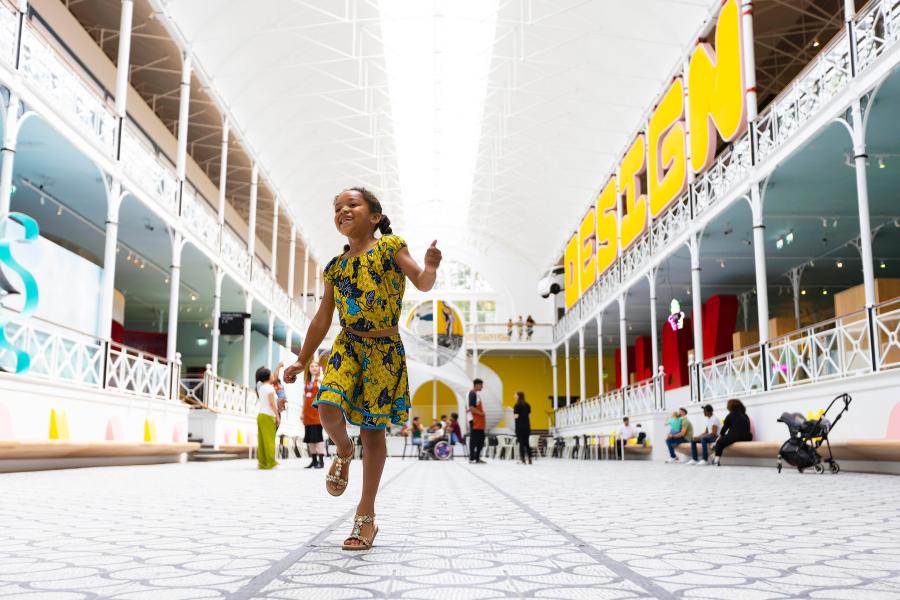 A young girl is happily running through the main lobby of the Young V&A Museum in London