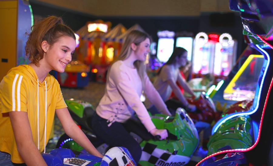 Two girls ride a motorcycle belonging to an arcade game at iPlay America