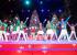 Darsteller auf der Bühne in festlichen Weihnachtskostümen und im Hintergrund in der Mitte Snoopy-Maskottchen im Weihnachtsmannkostüm, das ebenfalls bei einer Weihnachtsshow im King's Dominion auftritt