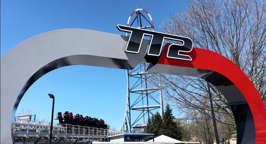 Top Thrill 2 roller coaster entrance sign at Cedar Point, with the coaster vehicle in the background