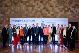 Les participants au Forum de Rhodes prennent une photo ensemble à l'intérieur, devant une bannière du Forum de Rhodes.